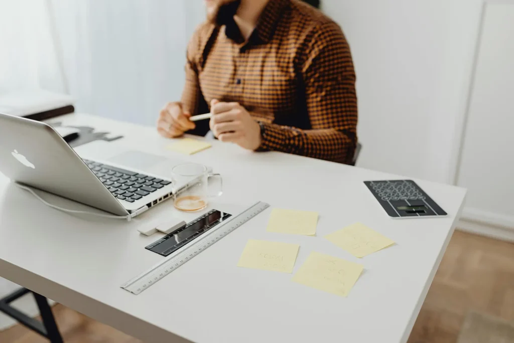 Business professional at a white desk with laptop, ruler, notes, and coffee cup, organising ideas on sticky notes