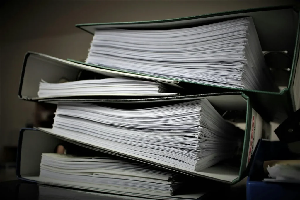Pile of overfilled lever-arch folders packed with documents, representing paperwork and record storage