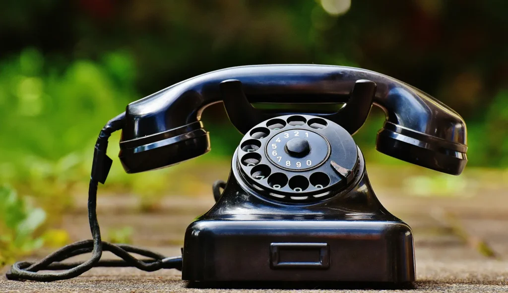 Classic black rotary dial telephone with numbered finger wheel resting on a wooden surface outdoors with blurred green background
