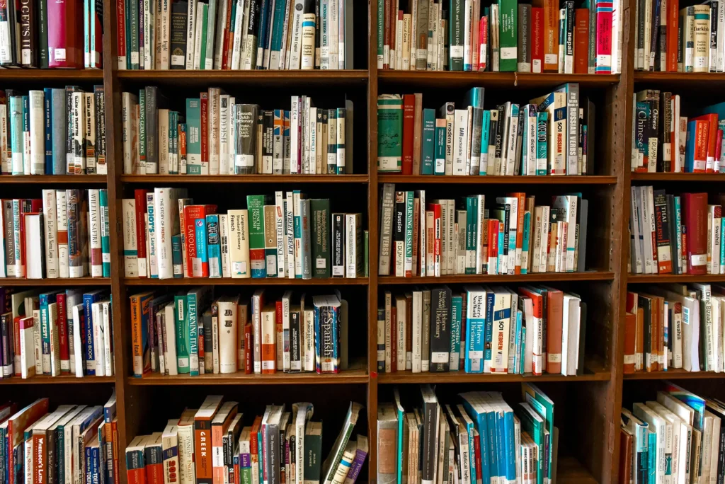 Extensive book collection organized on wooden library shelves, showing rows of colorful hardback and paperback titles across multiple shelves